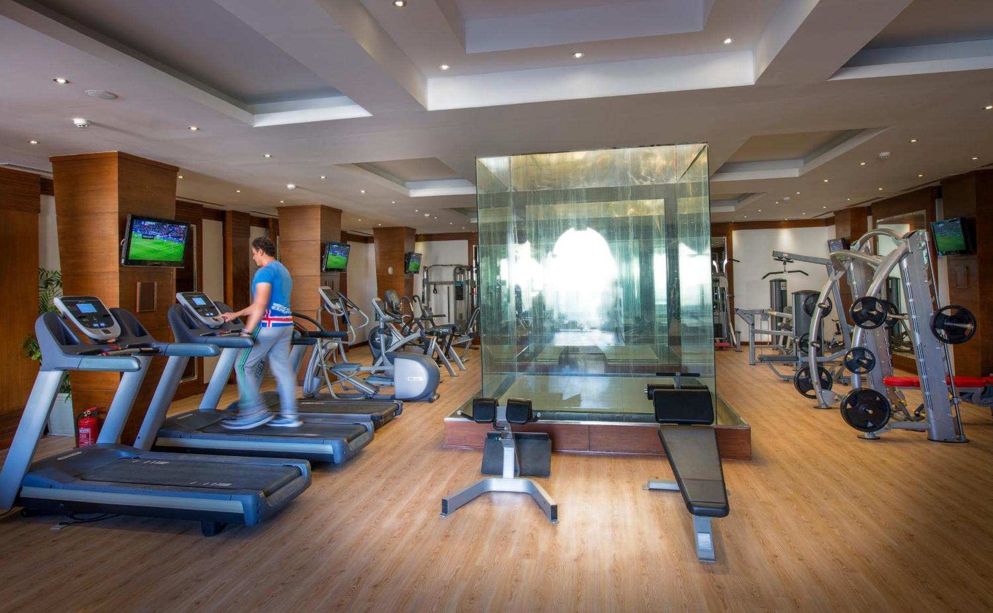 Sunrise Arabian Beach Resort Sharm el-Sheikh Exterior photo The photo shows a modern gym with various exercise equipment. On the left side, there are treadmills, with a person walking on one of them. In the center, there's a glass-walled space, which likely serves as a private area for workouts or classes. Th